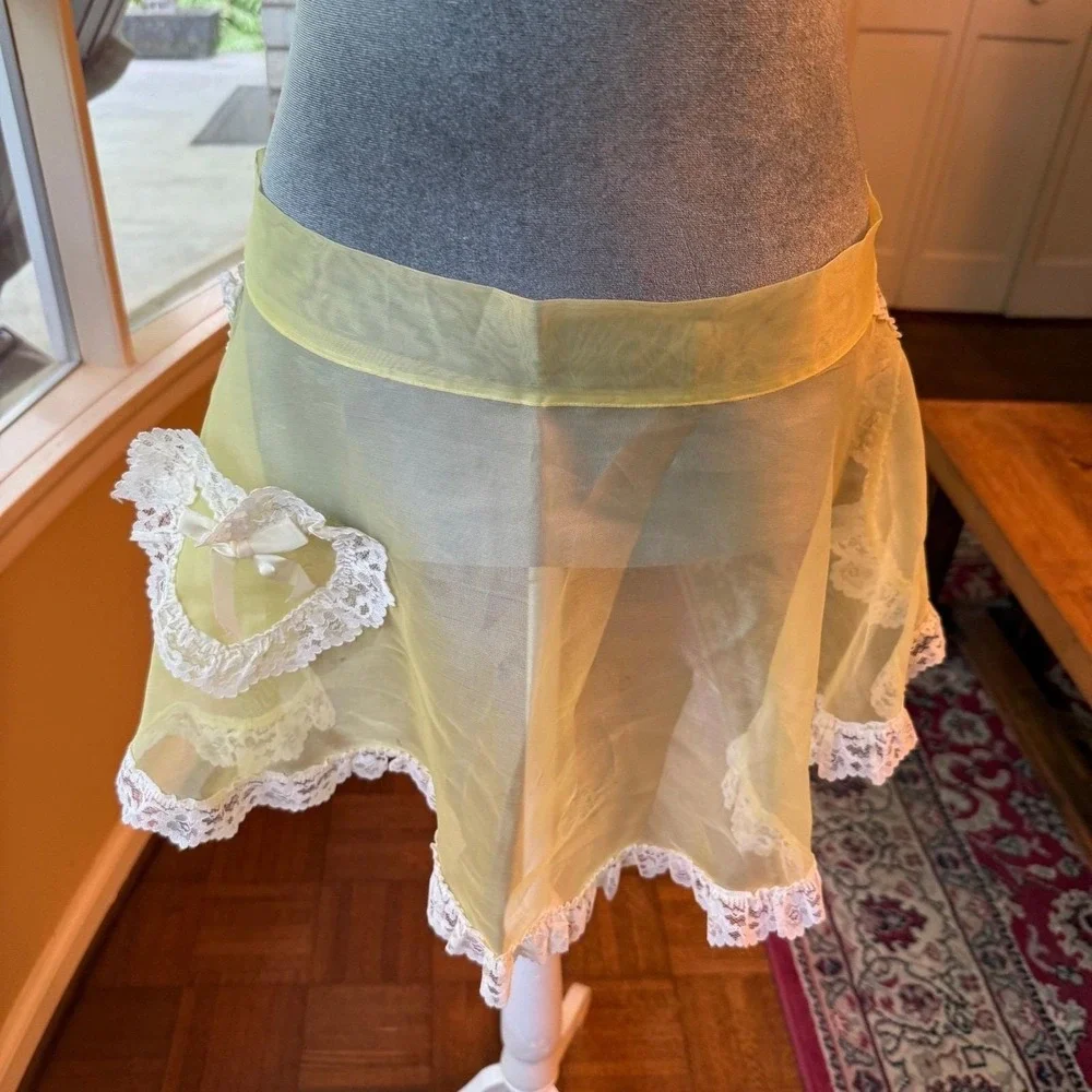 Vintage sheer yellow apron with ornate white lace trim and a bow-accented pocket